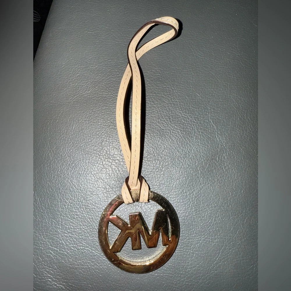 Michael Kors Gold Tone MK Logo Charm With A Light Tan/Creme Color Leather Tassel